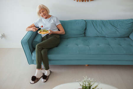 Aged woman eating on sofa at homeの写真素材