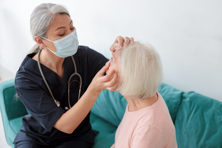 Female doctor examining eyes of elderly woman at homeの写真素材
