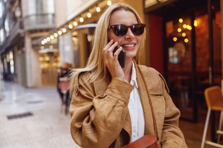 Portrait of lady in sunglasses calling by phone while standing on streetの写真素材