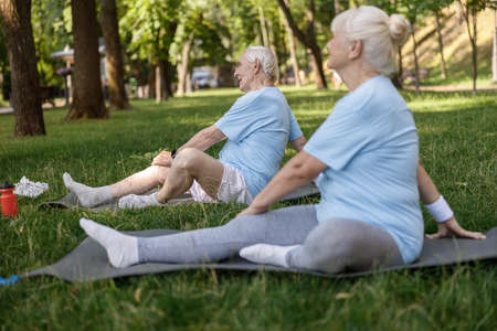 Senior family couple does yoga exercises sitting on lush lawn in picturesque parkの写真素材
