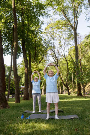 Positive man and woman do yoga on lush lawn in parkの写真素材