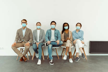 Colleagues in face masks sitting on chairsの写真素材