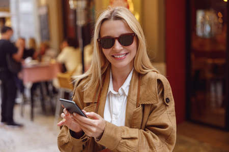 Beautiful female in sunglasses standing with phone near street restaurantの写真素材