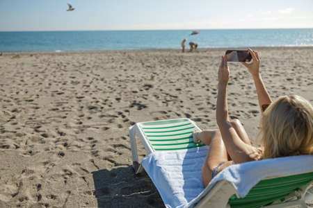 Woman taking selfie pictures using smartphone while sunbathing at beach