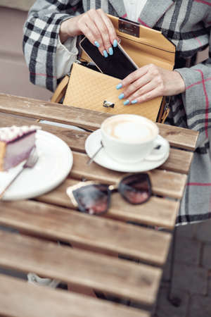 Top view on cappuccino cup , cheesecake on plate on table. Female with smartphone and bag.