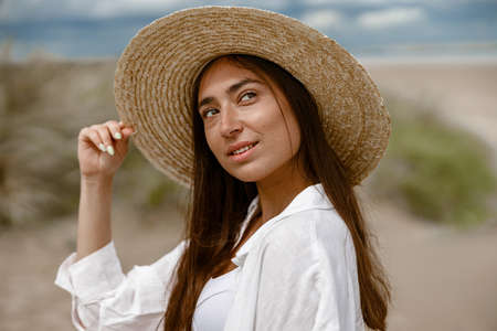 Close up of cheerful woman traveler with straw hat walking on beach during vacationの写真素材