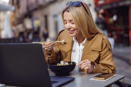 Woman eating food using chopsticks in street cafeの写真素材