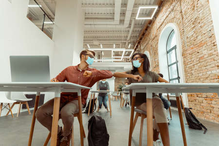 Students siting and greeting bumping elbows at workplace