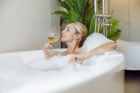 Side view on young beautiful Caucasian female enjoying white wine and taking bath. Bathroom.の写真素材