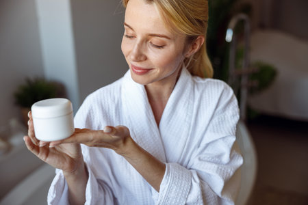 Attractive blonde young female demonstrating facial cream or body lotion. Skincare routine.の写真素材