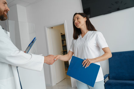Two doctors in uniform shaking hands standing in clinic hall near receptionの写真素材