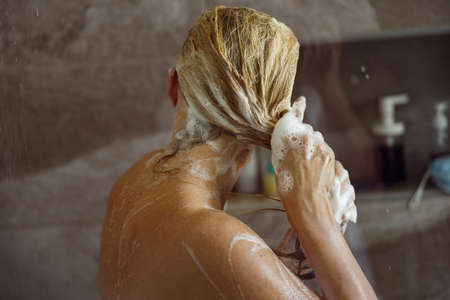 Close up of blonde Caucasian female foaming hair and washing with shampoo in shower.の写真素材