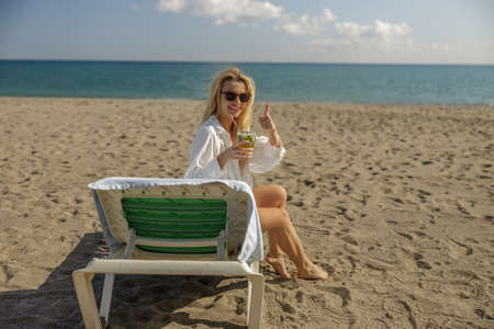 Content lady on vacation showing thumbs up at camera, drinking cocktail and sunbathing on a deck chairの写真素材