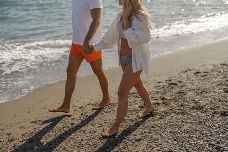 Cropped shot of young couple walking near the sea waves in swimsuitの写真素材