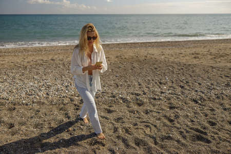 Full length shot of woman on vacation using phone while spending time on a beachの写真素材