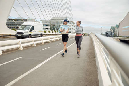 Two athletic women in sportswear is jogging on a bridge and listening music. Reaching the goalの写真素材