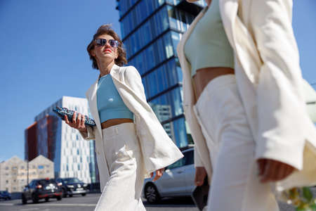 Two happy woman in trendy outfits laugh and walk outside on background of modern buildingの写真素材