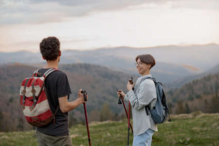 Cheerful woman with walking sticks standing on peak of munt with boyfriend or friend.の写真素材