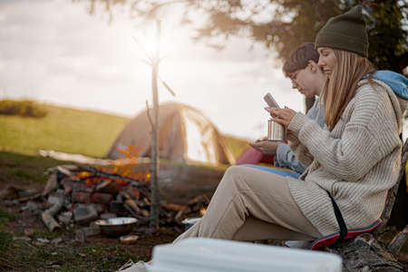 Caucasian females sitting at fire in camp site and using phones when resting. Travelers.の写真素材