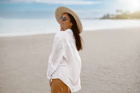 Beautiful woman traveler in a hat standing on tropical beach and looking away. Vacation conceptの写真素材