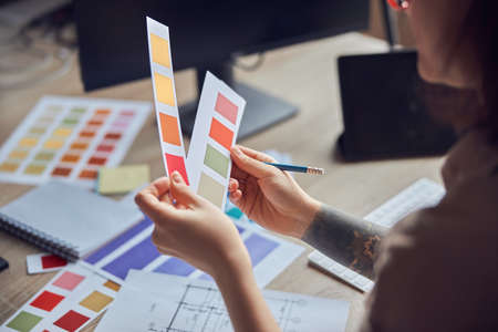 Close up shot of hands of female interior designer working on a project, holding color samples,...