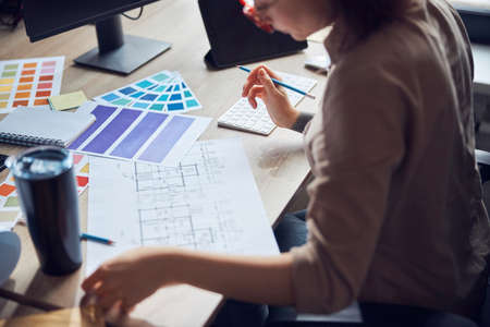 Cropped shot of female interior designer working on a project with bluepint and color samples,...