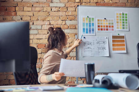 Busy woman designer attaching blueprint paper and color samples on board while working on new interior design project in her officeの写真素材