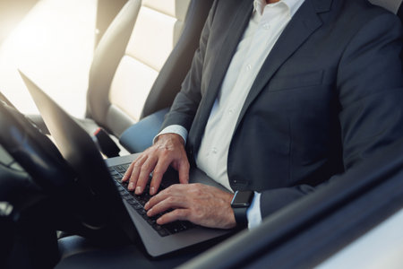 Close up of businessman working on laptop while sitting on driver seat in luxury carの写真素材