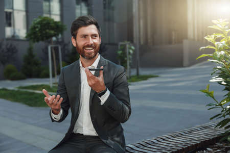 Businessman recording audio message to client sitting near office during breakの写真素材