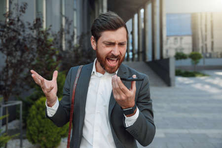 Emotional Businessman recording audio message to client standing near office