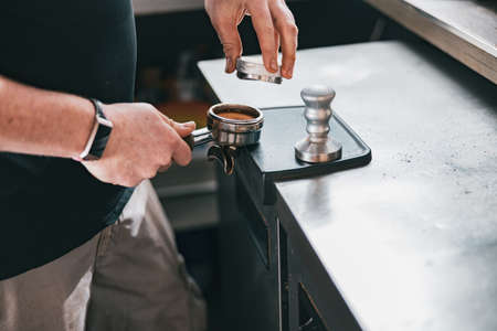 Barista holding tamper and press ground coffee in holder to make espresso for clientの写真素材