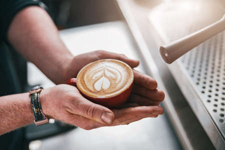 Close up of male Barista hands holding fresh made cappuccino or latte cup in coffee shopの写真素材
