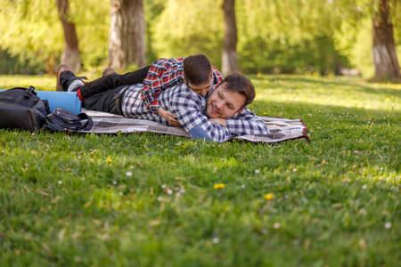 Happy father resting in park and little son lying on back of daddy. Relaxation with child.の写真素材