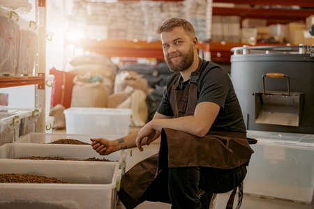 Smiling Male barista in uniform inspection freshly roasted coffee beans on manufacturingの写真素材
