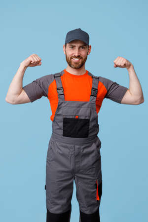 Positive man builder in uniform showing his biceps at camera and smile. Studio shoot