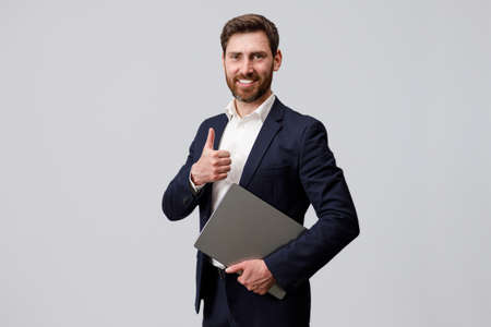 Smiling businessman with bread holding laptop and showing thumb upの写真素材