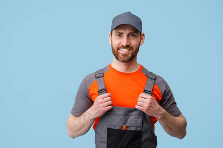 Portrait of smiling builder in uniform holding on his jumpsuit and looking at camera