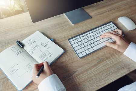 Close up of business woman hands working using keyboard of computer and making notes in office