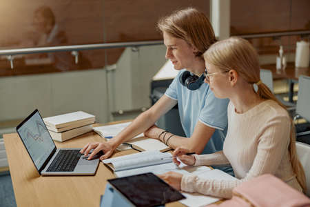 Two friends students with laptop and books studying in University Libraryの写真素材