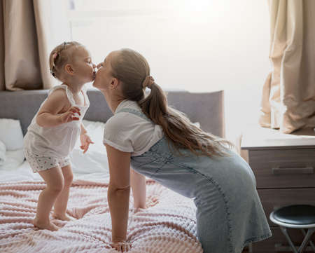 Young mother smiling and kiss her baby while lying in bed at homeの写真素材