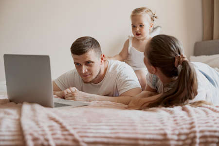 Cheerful family having fun together watching cartoons online on laptop lie on sofa at homeの写真素材