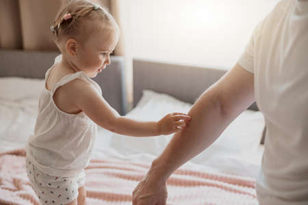 Close up of smiling baby girl touch daddys hand standing on bedの写真素材