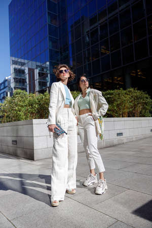 Two fashionable woman friends standing on background of modern buildingsの写真素材
