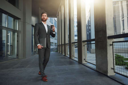 Attractive european businessman with coffee and laptop near office building during breakの写真素材