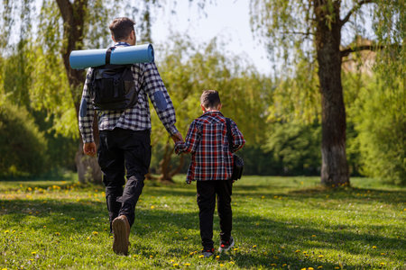 Rear on Caucasian father and little son with backpack walking the park or forest on summer day.の写真素材