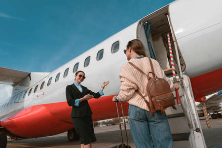 Woman stewardess standing near airplane and inviting female passenger on board