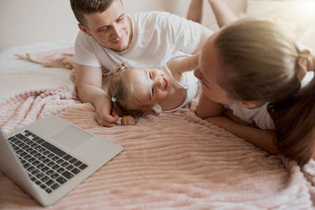 Cheerful family having fun together watching cartoons online on laptop lie on sofa at home