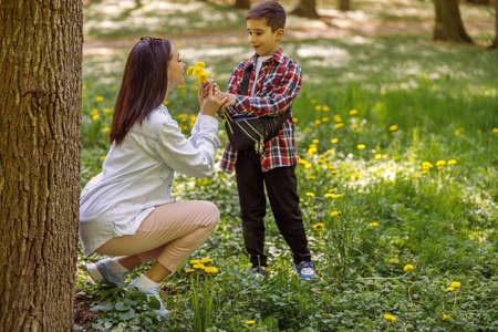 Pretty mother smelling flowers from small son in park. Woman with dandelions and child.の写真素材