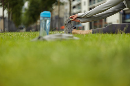 Close up of woman doing stretching exercise on green grass at city park