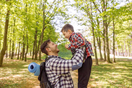 Cheerful Caucasian man holding his small cute son in hands high. Rising kid. At forest.
